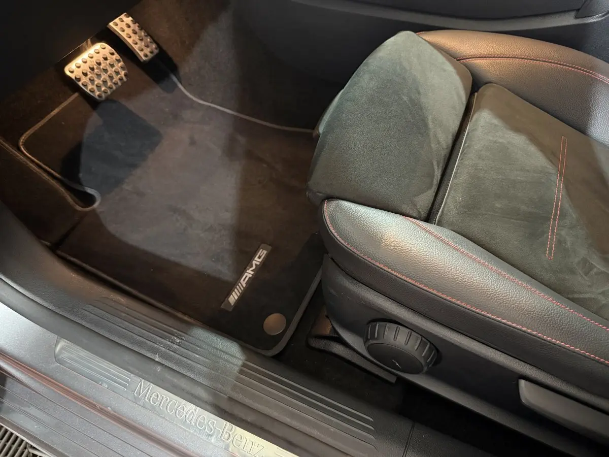 Vue intérieure côté conducteur sur le siège AMG noir avec surpiqûres rouges et seuil de porte Mercedes-Benz gris foncé.