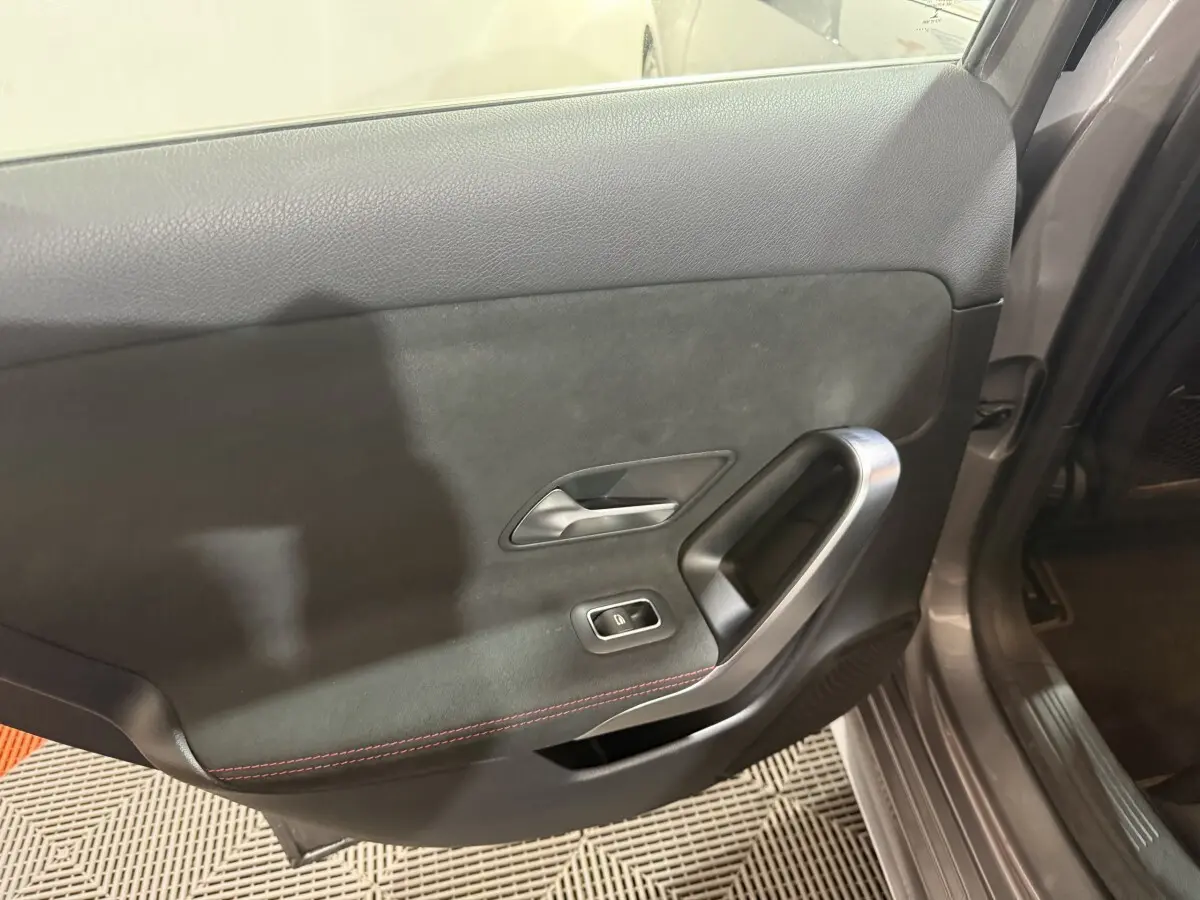 Vue intérieure côté gauche de la porte arrière grise foncée de la Mercedes Classe A 200 AMG Line avec surpiqûres rouges.