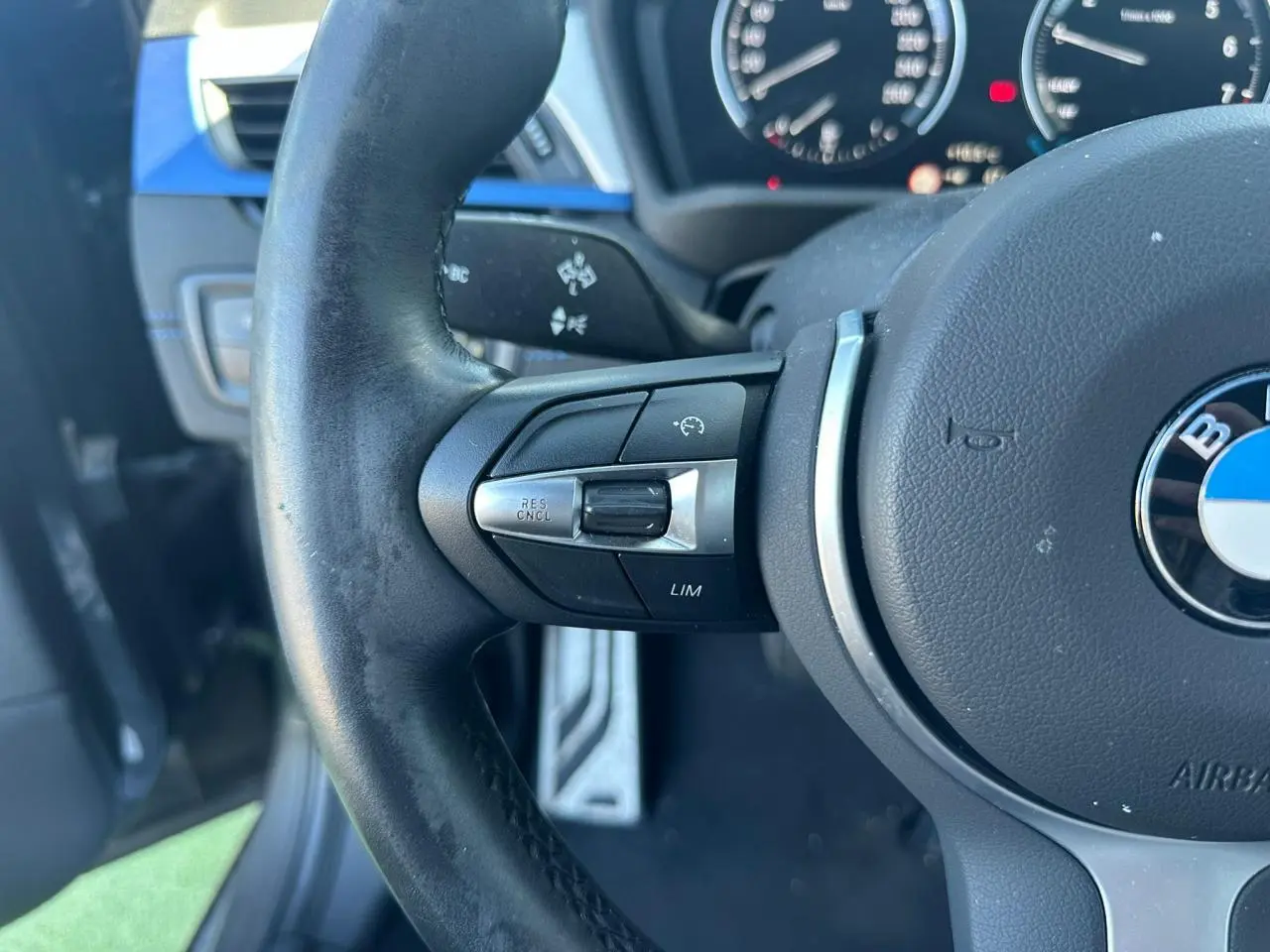 Gros plan sur le volant cuir M de BMW X2 gris foncé, avec commandes multifonctions et tableau de bord flou en arrière-plan.