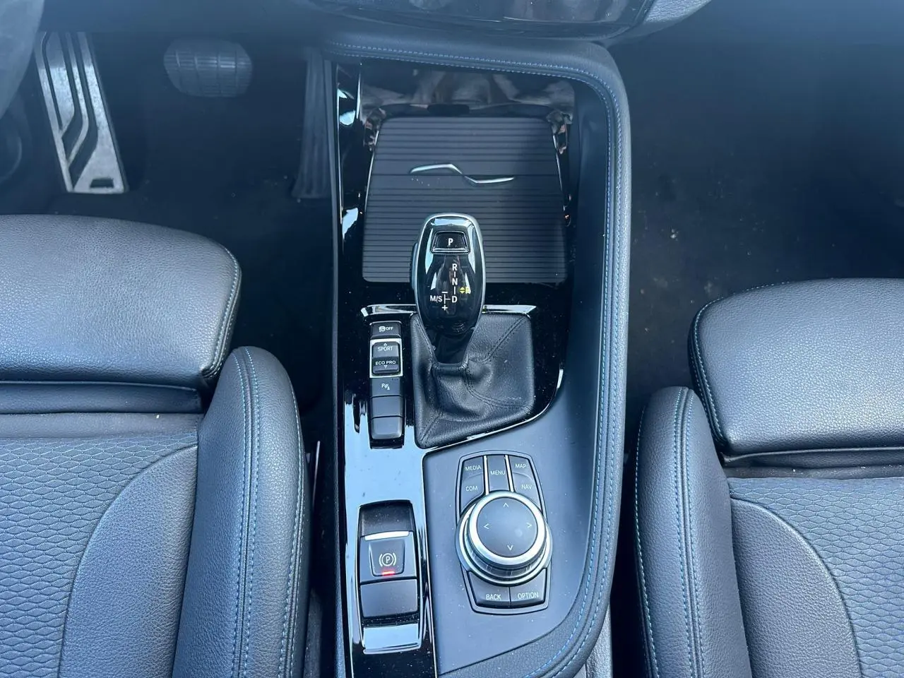 Vue plongeante sur la console centrale noire brillante du BMW X2 avec levier de vitesses automatique et commandes de mode de conduite.