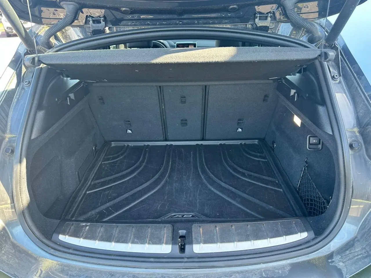 Coffre ouvert vu de l'arrière d'un BMW X2 gris foncé avec tapis de protection et filet latéral.
