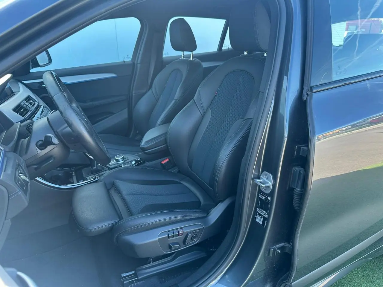 Vue intérieure côté conducteur d'une BMW X2 gris foncé, mettant en valeur les sièges sport en tissu et similicuir avec réglages électriques.