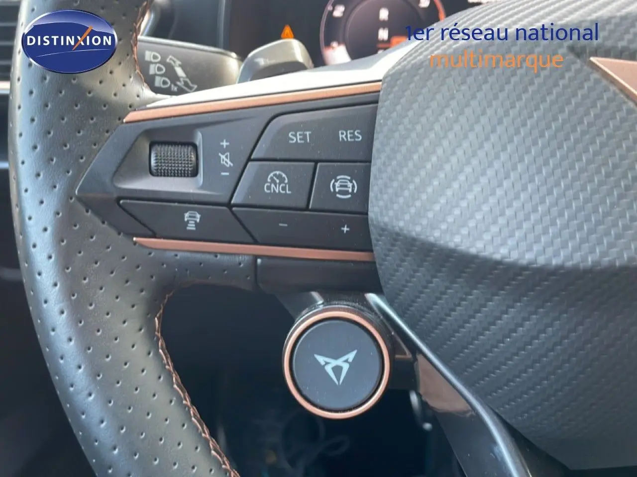 Gros plan sur le volant en cuir perforé avec commandes intégrées et logo CUPRA au centre, intérieur noir.