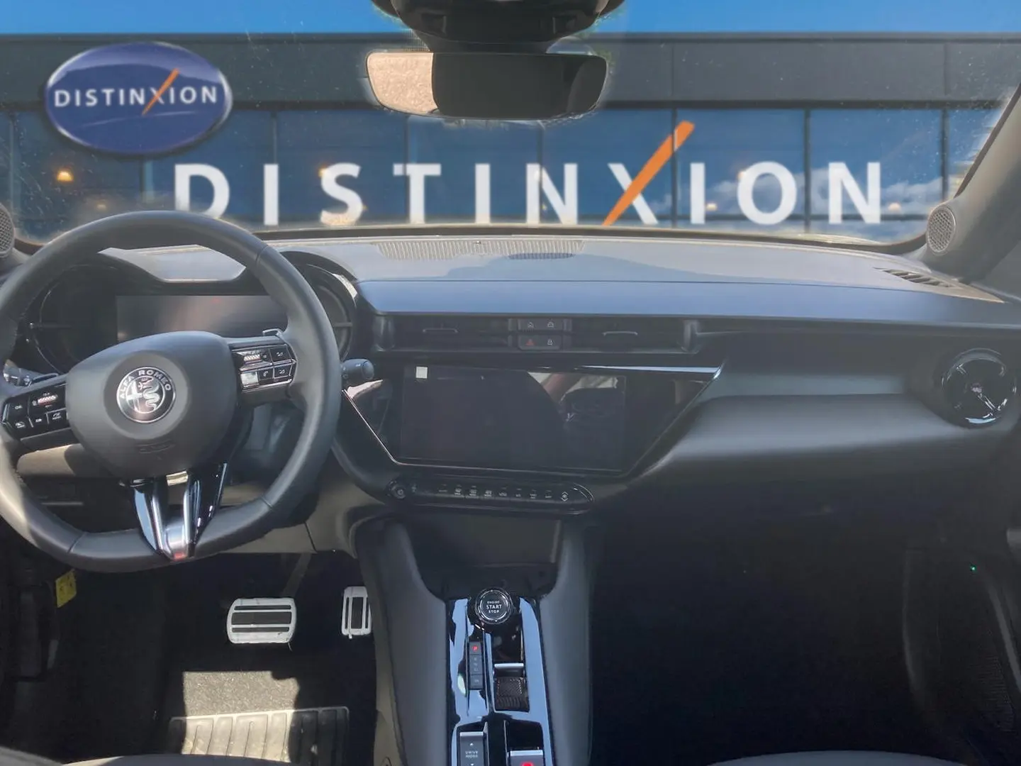 Vue intérieure avant de l'Alfa Romeo Junior 1.2 hybride 2026, tableau de bord et volant noir avec écran tactile central.