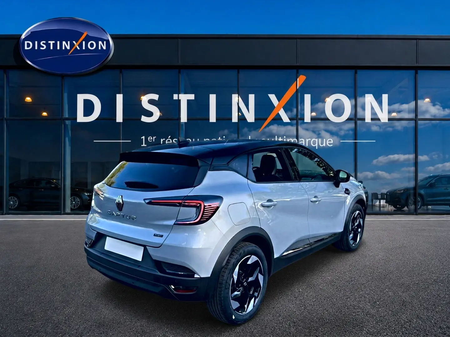 Vue 3/4 arrière droite du Renault Captur gris rafale avec toit noir et jantes alu noires devant une vitrine Distinxion.