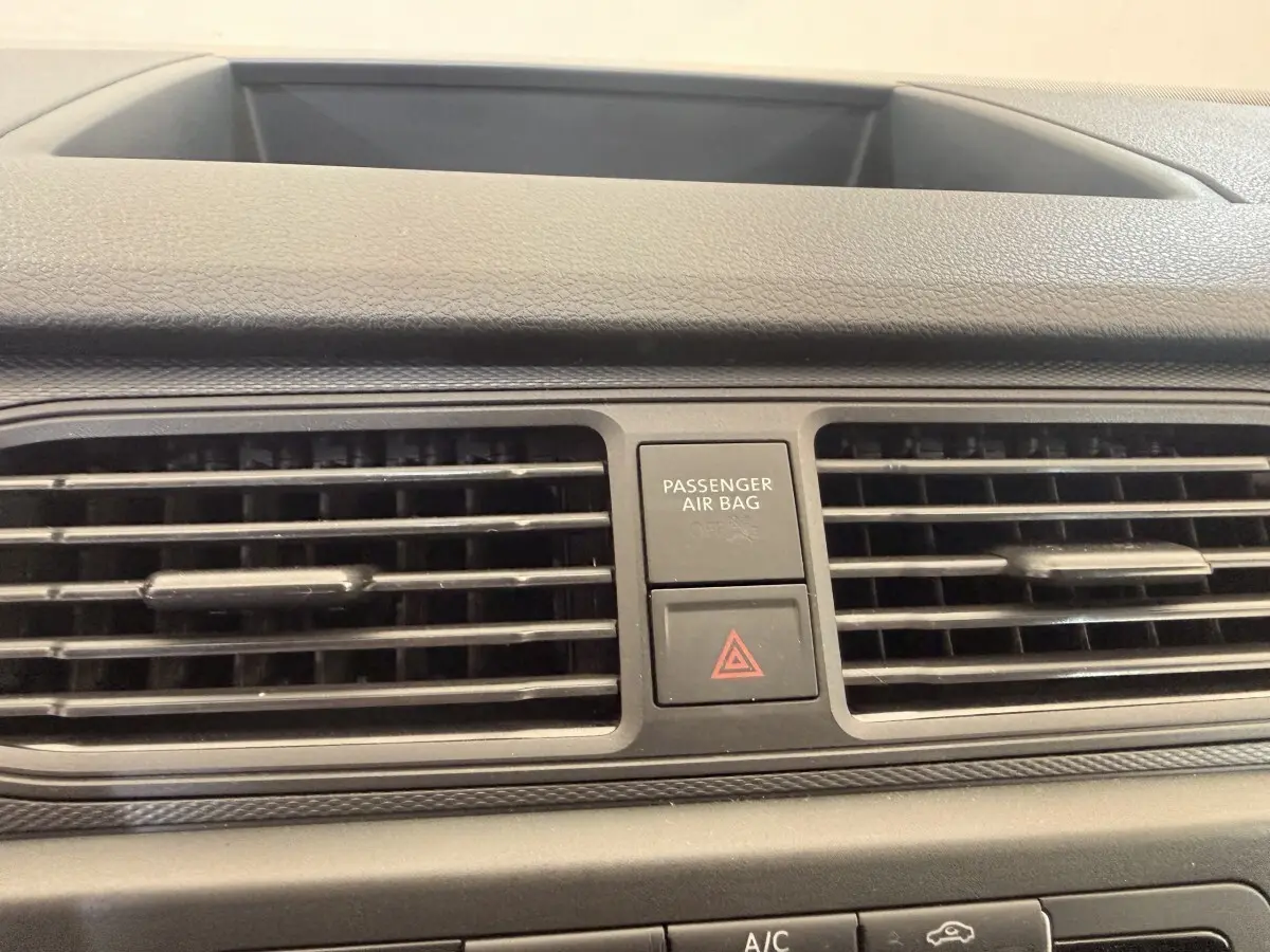 Gros plan sur la grille d’aération centrale et les boutons de sécurité du tableau de bord du Volkswagen Caddy noir.