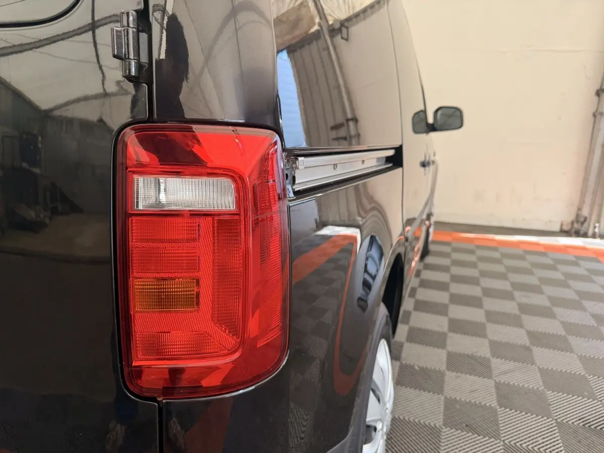 Feu arrière gauche en gros plan du Volkswagen Caddy noir, vue latérale arrière droite dans un garage.