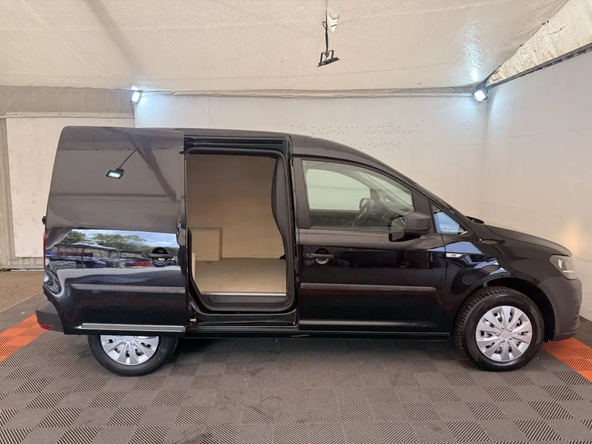 Profil droit d’un Volkswagen Caddy noir 2019 avec porte coulissante ouverte montrant l’espace de chargement vide.