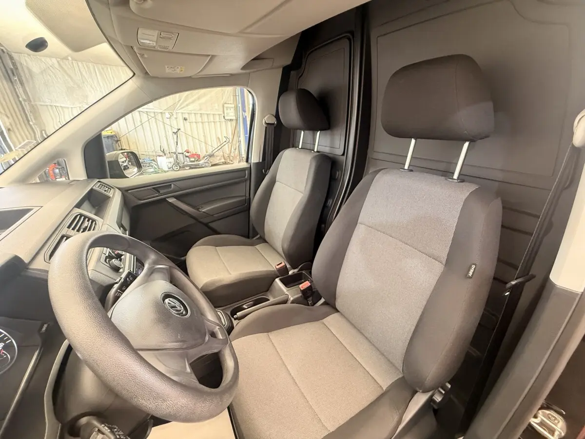 Vue intérieure avant du Volkswagen Caddy 2019 noir, montrant les sièges tissu gris et la cloison pleine noire derrière.