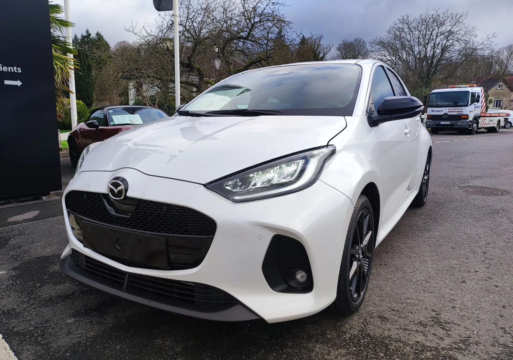 Vue 3/4 avant droite d'une Mazda2 Hybrid blanc métallisé avec calandre noire et jantes foncées au design sportif.