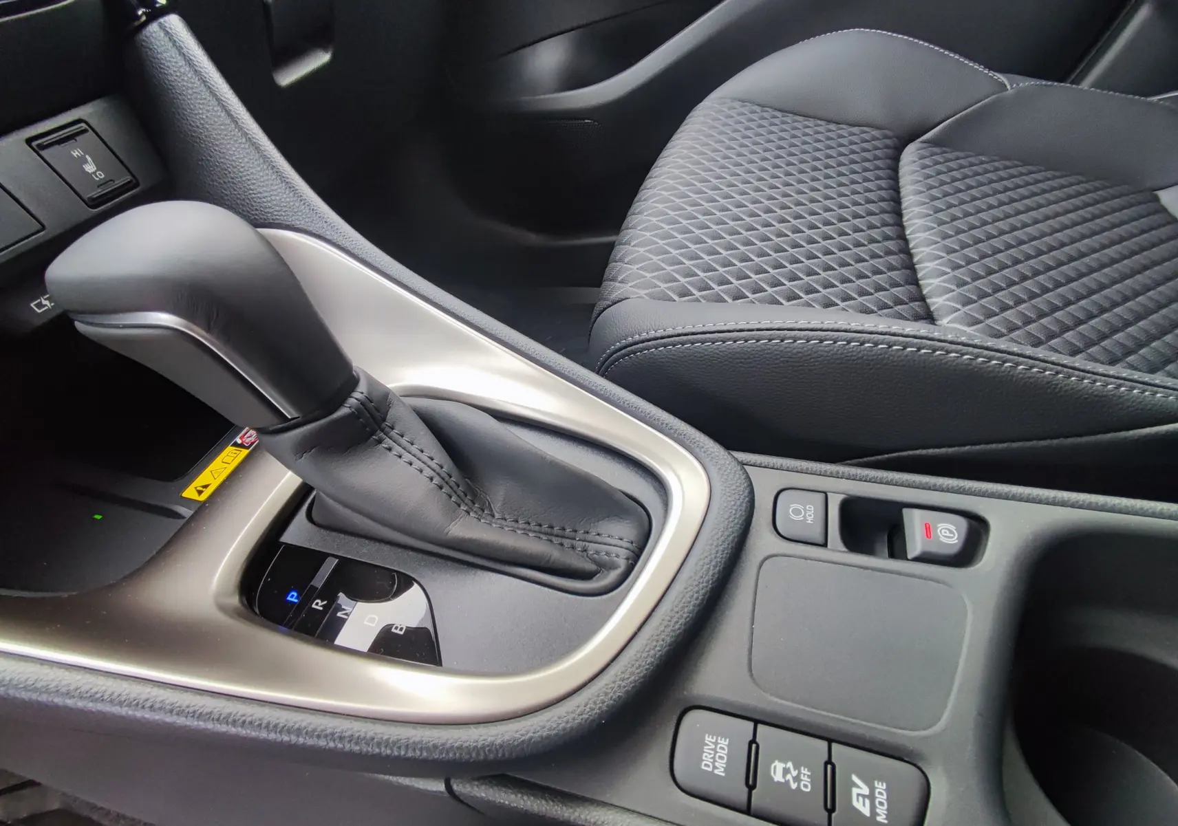 Gros plan sur la console centrale de la Mazda2 Hybrid 2024, montrant le levier de vitesse automatique et les boutons de mode de conduite.