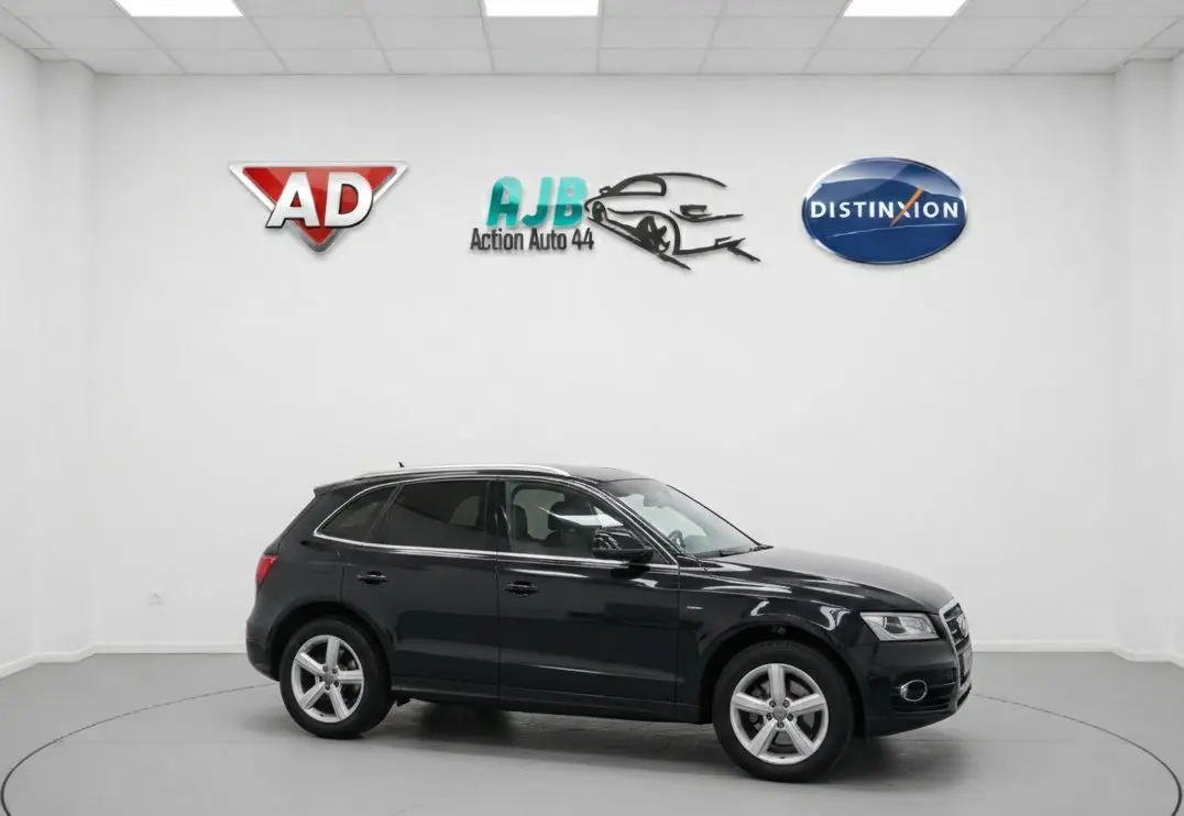 Audi Q5 noir vue de profil côté gauche dans un studio avec logos de concessionnaires en arrière-plan.
