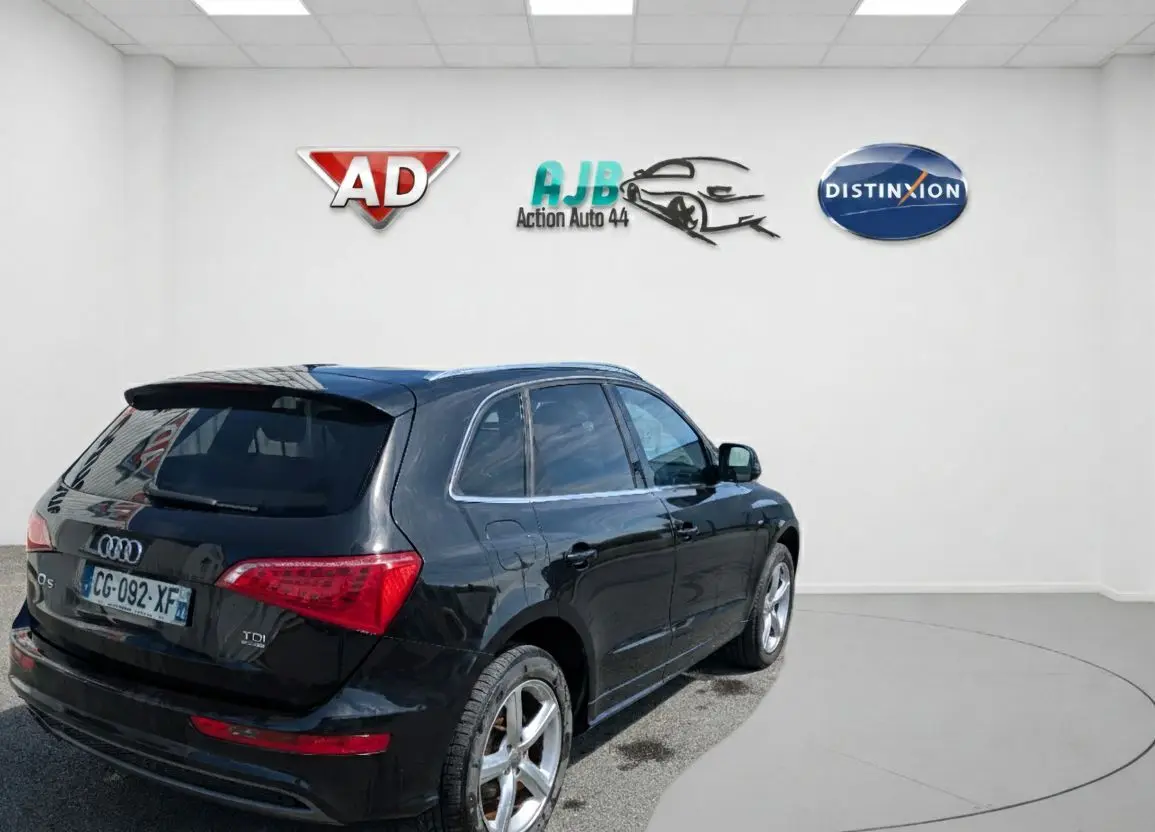 Audi Q5 noir vue 3/4 arrière droit dans un showroom, avec jantes alliage et feux arrière LED distinctifs.