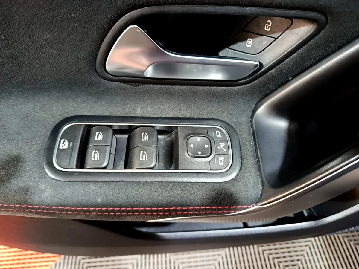 Gros plan sur la commande des vitres et rétroviseurs côté conducteur d'une Mercedes Classe A noire, avec surpiqûres rouges.