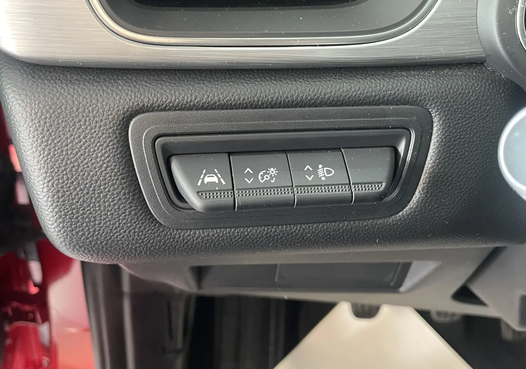 Gros plan sur les commandes de réglage d'assistance et d'éclairage du tableau de bord d'un Renault Captur rouge, vue intérieure côté conducteur.