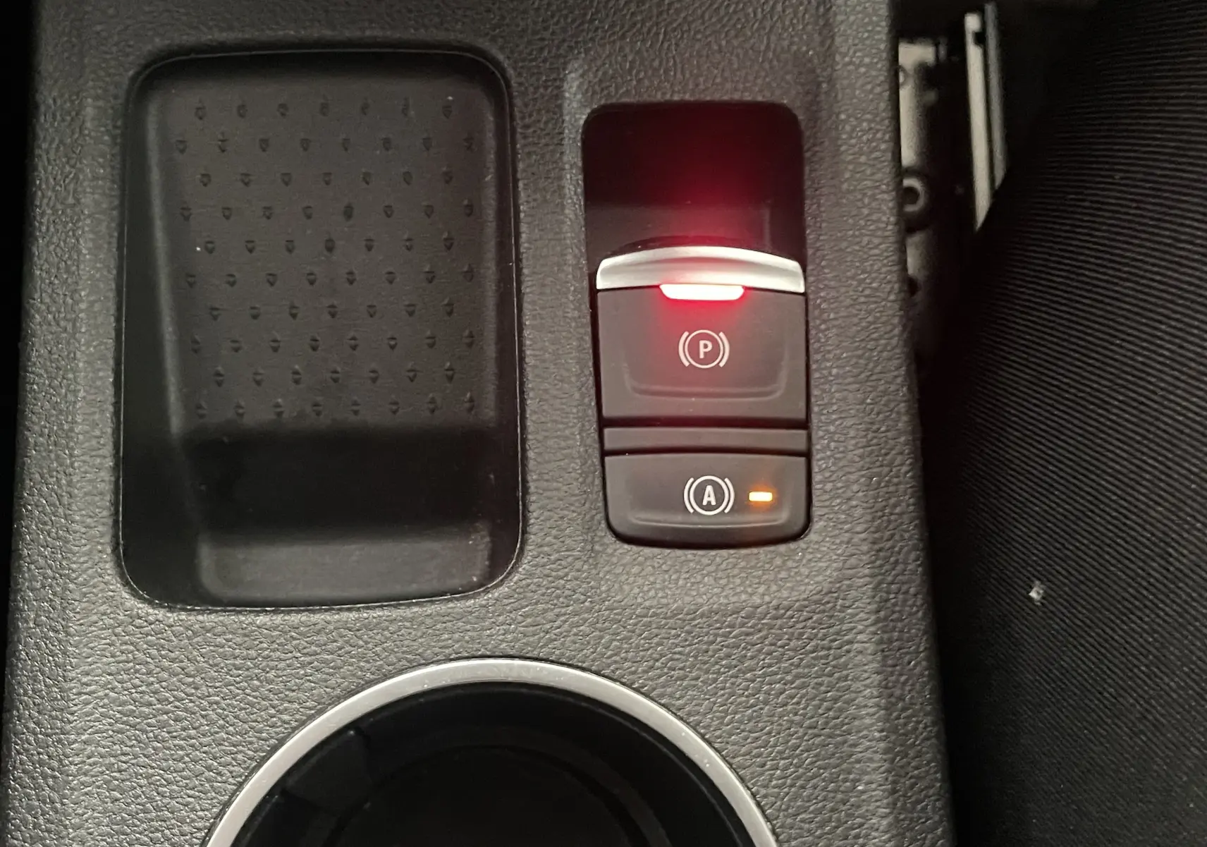 Gros plan sur la console centrale noire du Renault Captur rouge, avec bouton frein à main électronique et arrêt auto allumés.