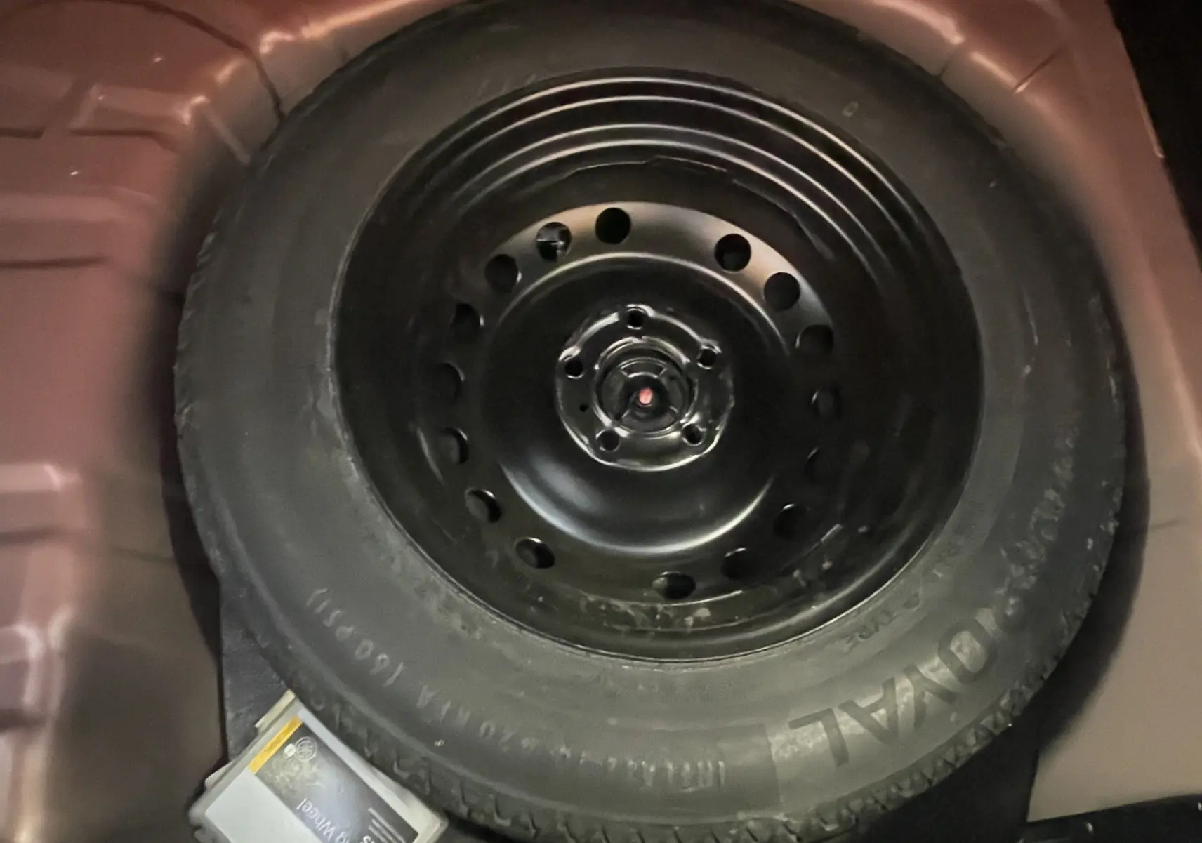 Gros plan sur la roue de secours noire logée dans le coffre rouge du Renault Captur 2019.