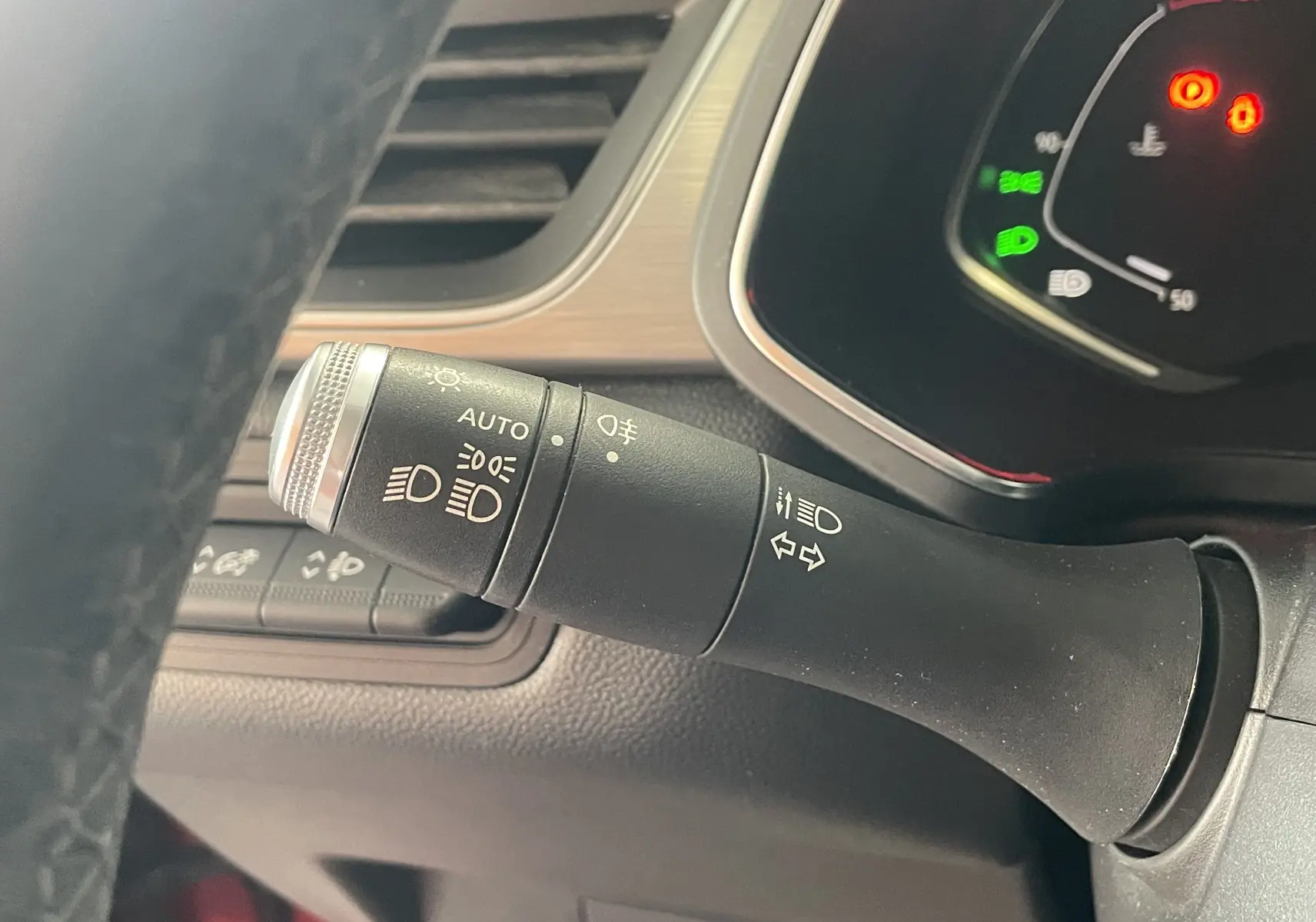 Gros plan sur la commande des feux et clignotants à gauche du volant d’un Renault Captur rouge, tableau de bord partiellement visible.