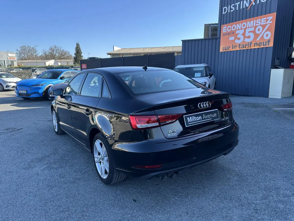 Audi A3 berline noire vue en 3/4 arrière droit, avec jantes aluminium et logo distinctif sur parking extérieur.