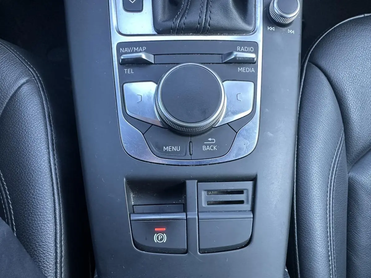 Vue plongeante sur la console centrale noire de l'Audi A3 2020 avec commandes multimédia et frein à main électrique.
