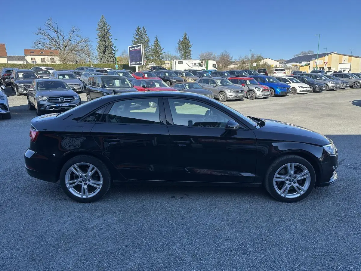 Audi A3 berline noire vue de profil côté gauche sur un parking en extérieur, jantes alliage 5 branches.