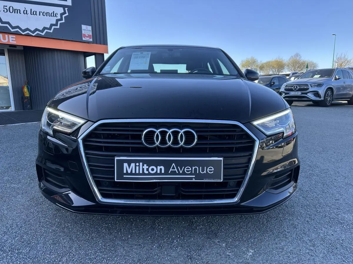 Vue frontale d'une Audi A3 berline noire 2020 avec calandre chromée et phares LED allumés, stationnée en extérieur.