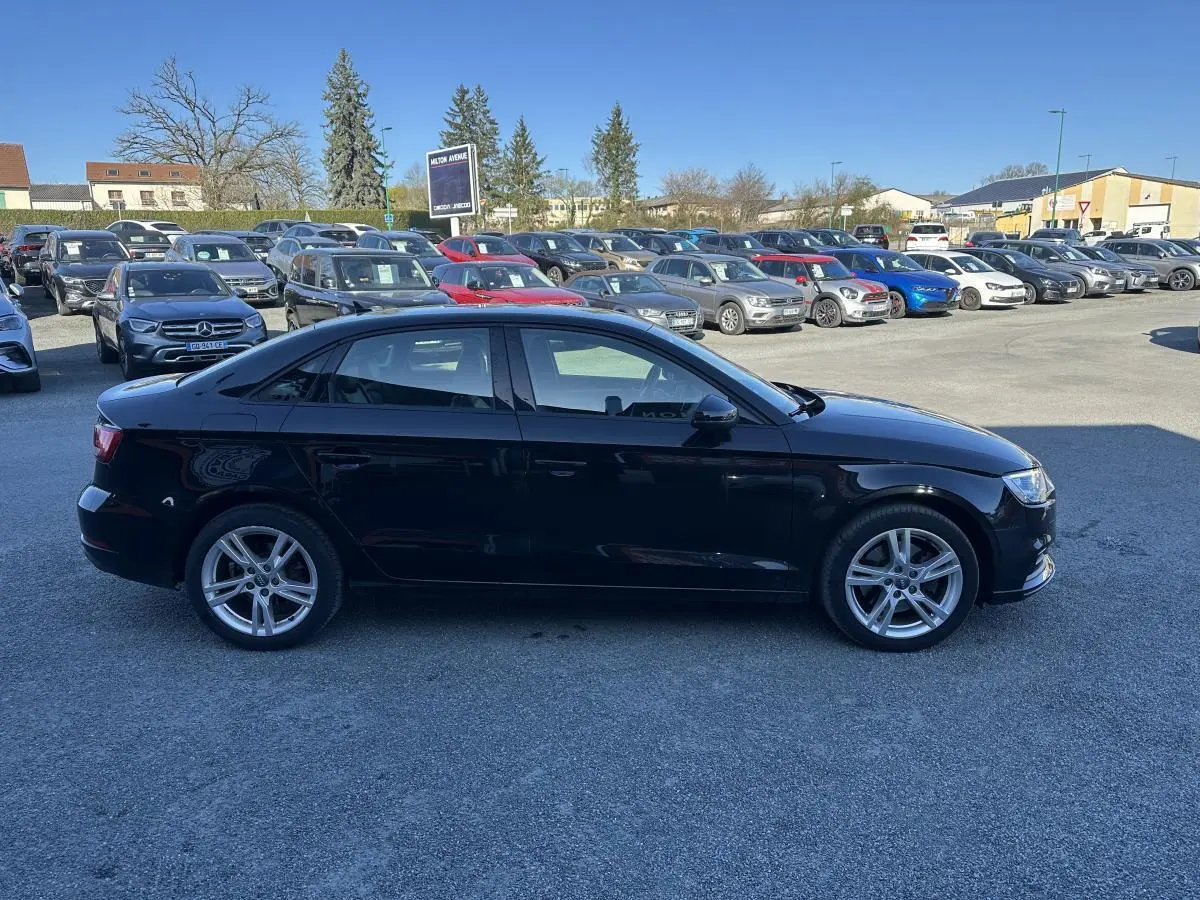 Audi A3 berline noire vue de profil côté gauche sur un parking en extérieur par temps clair.