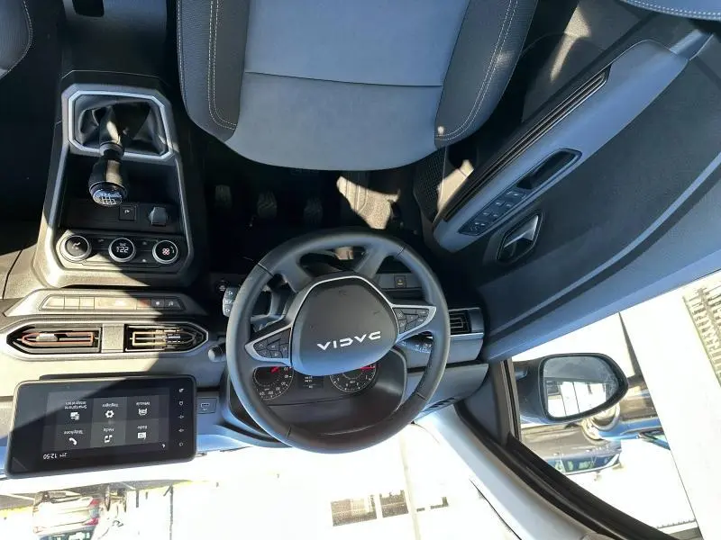 Vue intérieure de face du volant et console centrale du Dacia Jogger noir nacré, avec levier de vitesse manuel et écran tactile.
