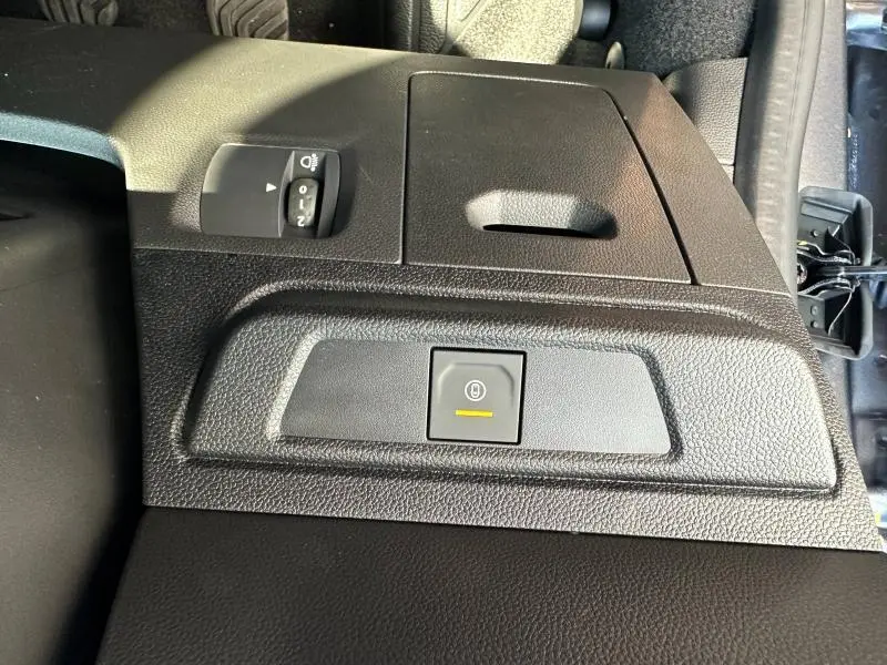 Détail du tableau de bord noir nacré du Dacia Jogger 2024 avec commande de frein à main électrique et réglage des phares.