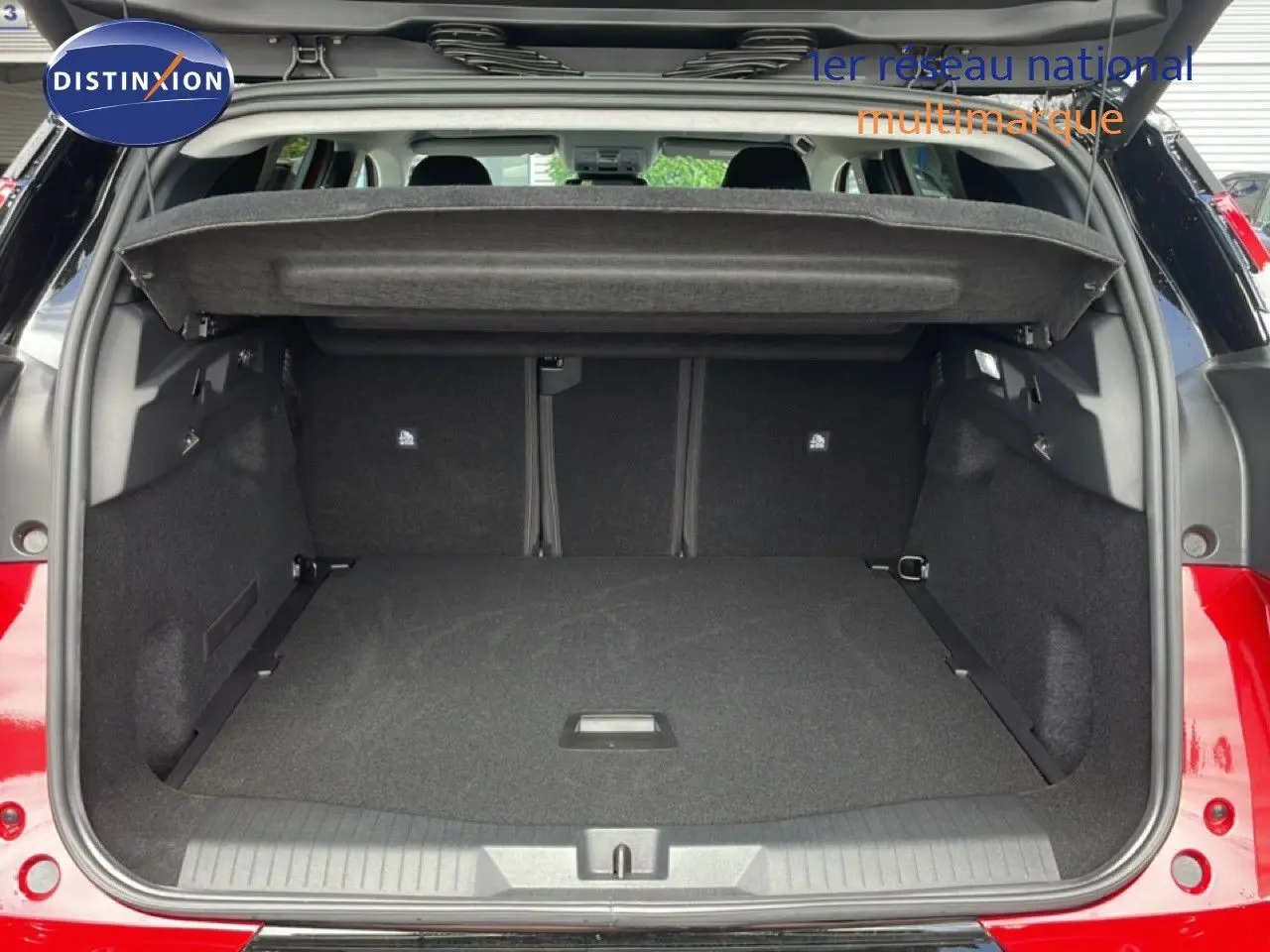 Coffre ouvert vu de l'arrière d'un Citroën C5 Aircross Hybrid rouge rubis métal, espace de chargement spacieux et tapis noir.