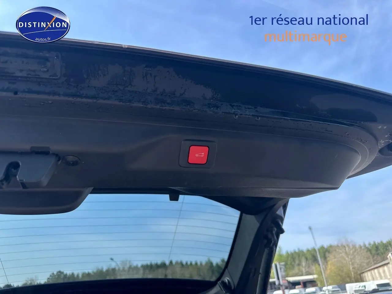 Vue depuis l'intérieur du coffre ouvert d'un Peugeot 3008 gris Artense, bouton rouge d'ouverture électrique visible sur le hayon.