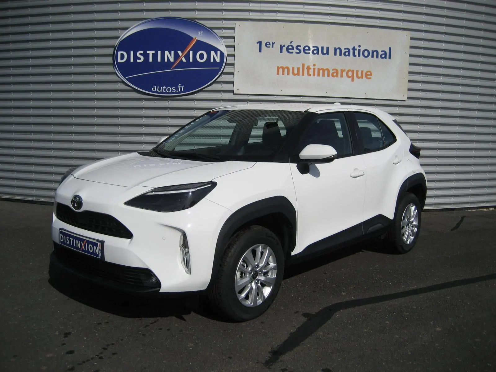 Toyota Yaris Cross blanc vue 3/4 avant droit, avec protections noires sur les passages de roues et jantes argentées.