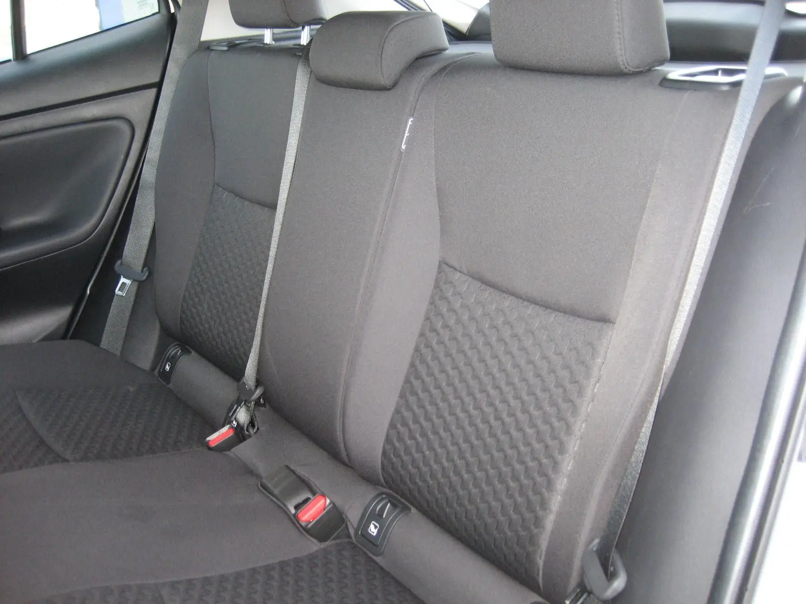 Vue intérieure des sièges arrière noirs en tissu texturé du Toyota Yaris Cross 2025, avec ceintures de sécurité visibles.