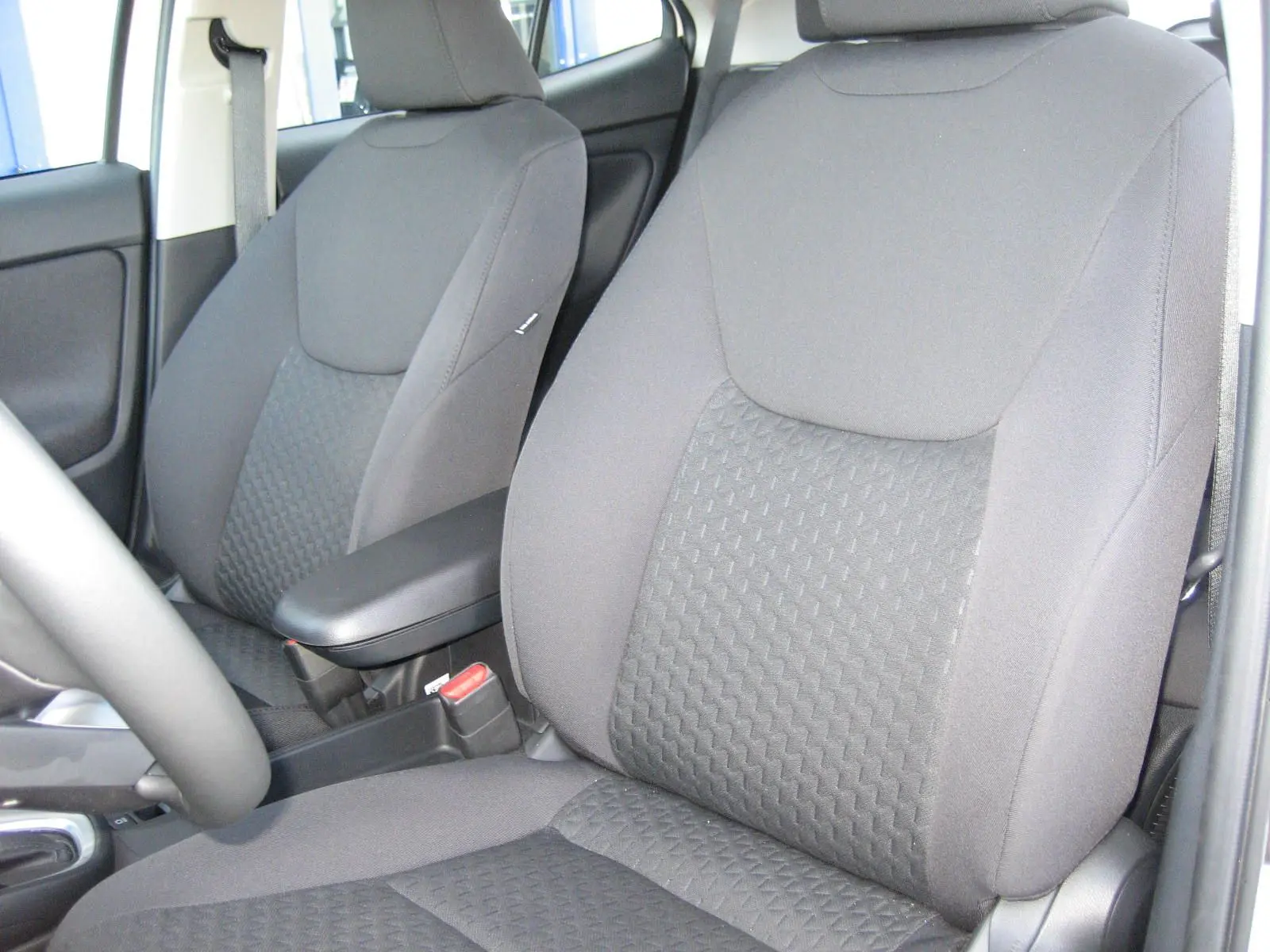 Gros plan sur les sièges avant noirs de la Toyota Yaris Cross 2025, mettant en valeur leur tissu texturé et l'accoudoir central.