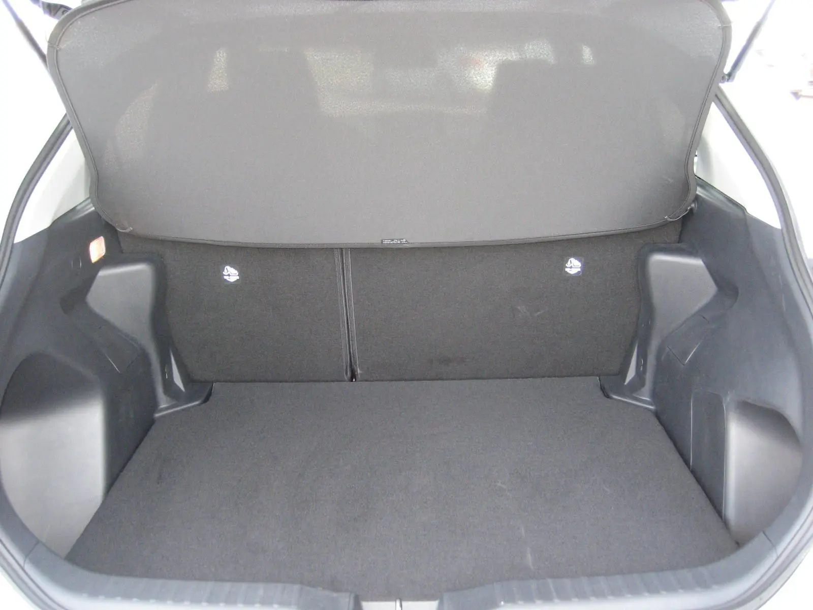Coffre ouvert vu de l'arrière d'une Toyota Yaris Cross blanche 2025, espace de chargement vide et tapis noir.