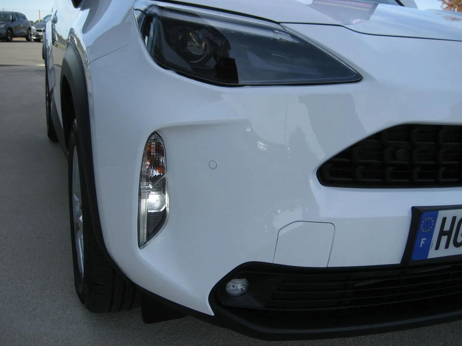Gros plan sur l'avant droit blanc d'une Toyota Yaris Cross 2025, mettant en valeur son phare et sa calandre noire.