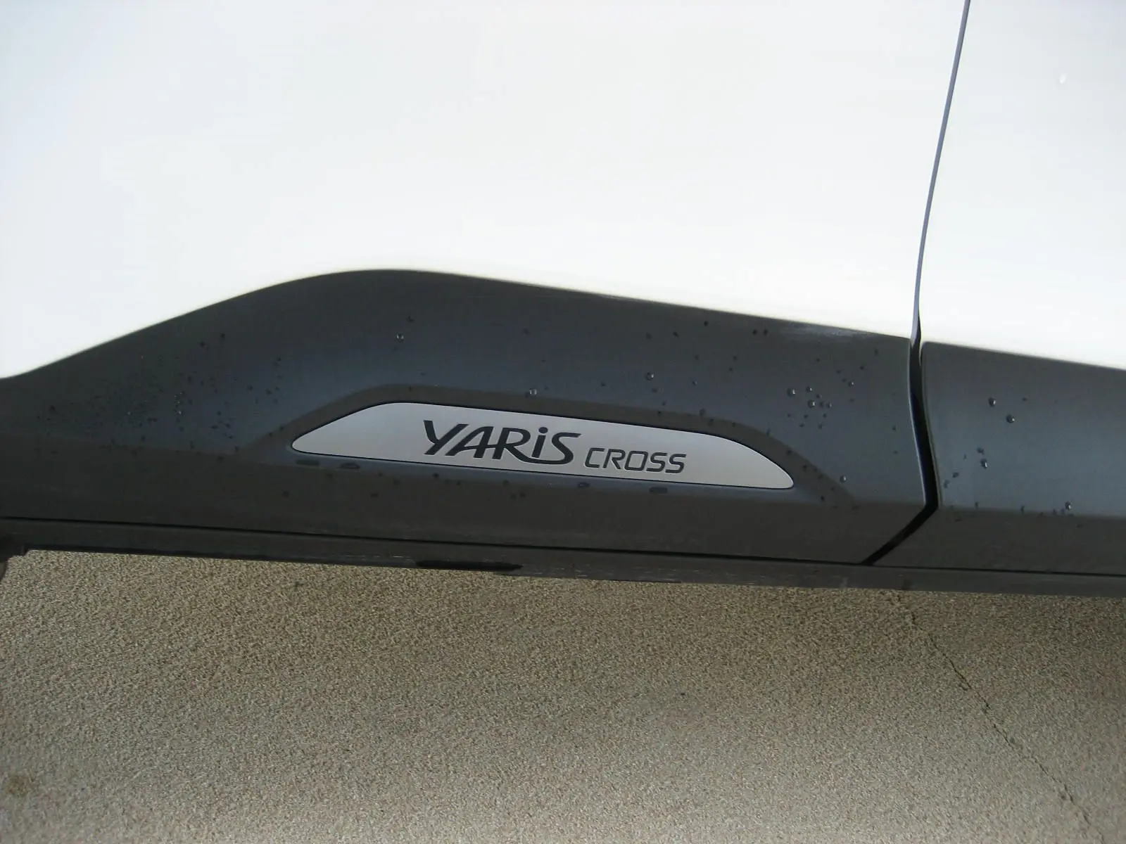 Gros plan sur la bas de caisse noir avec logo YARIS CROSS sur une Toyota Yaris Cross blanche.