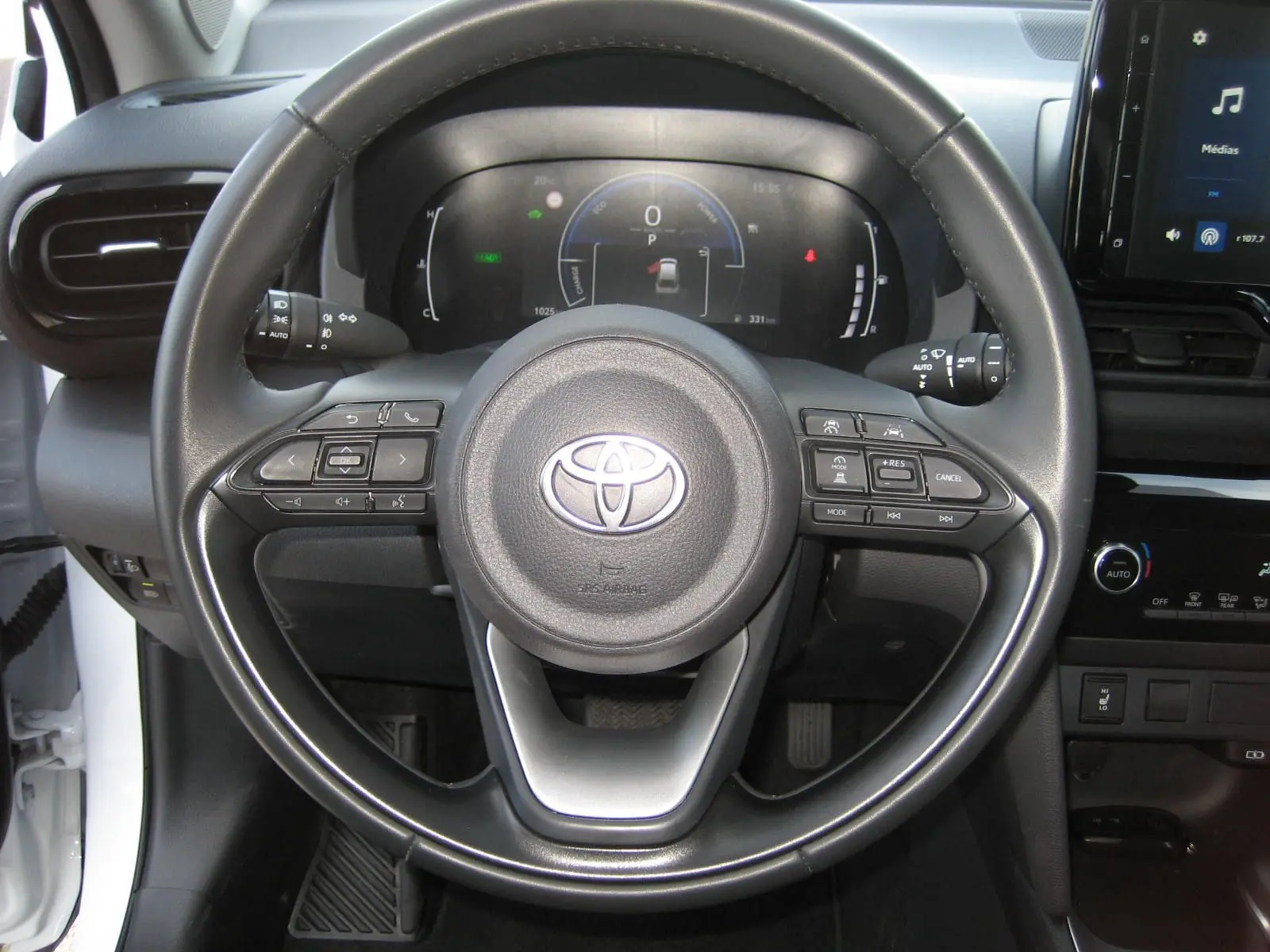 Vue centrée sur le volant noir de la Toyota Yaris Cross blanche 2025, avec tableau de bord digital et commandes intégrées.