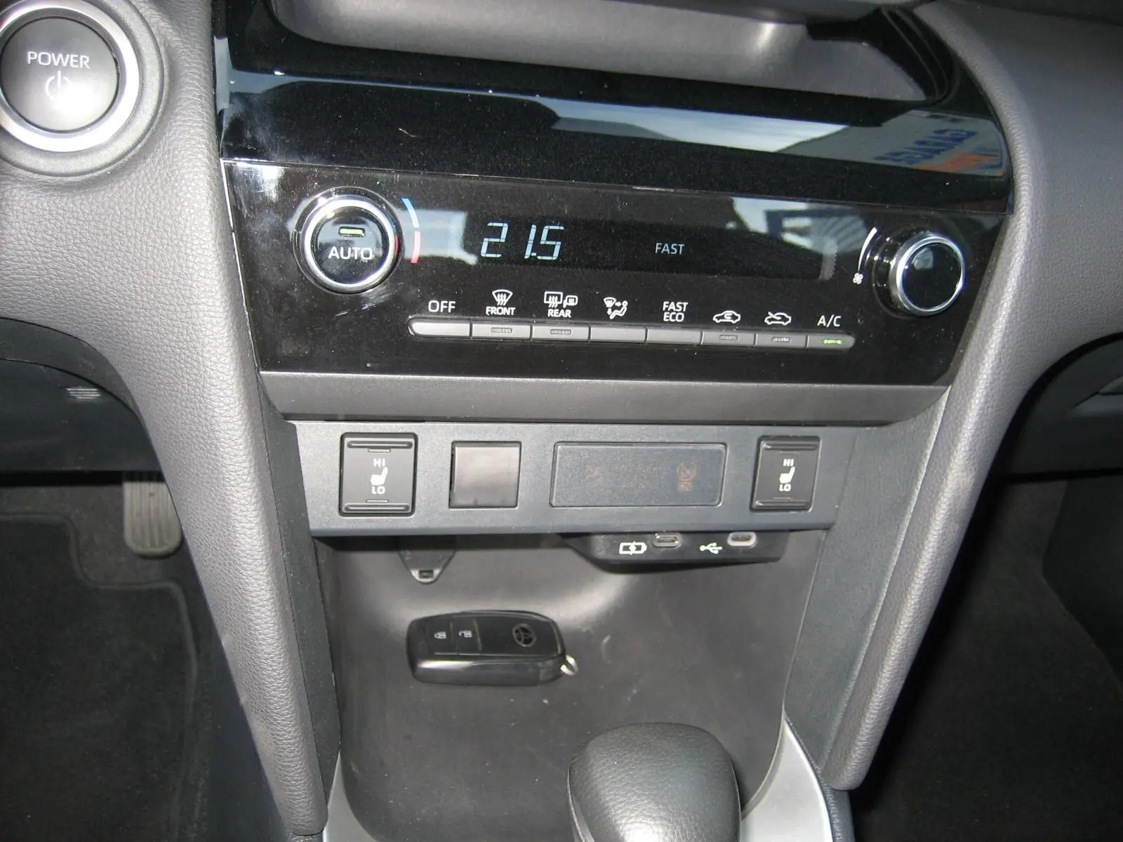 Vue rapprochée de la console centrale noire de la Toyota Yaris Cross blanche 2025, avec commandes climatisation et clé posée.