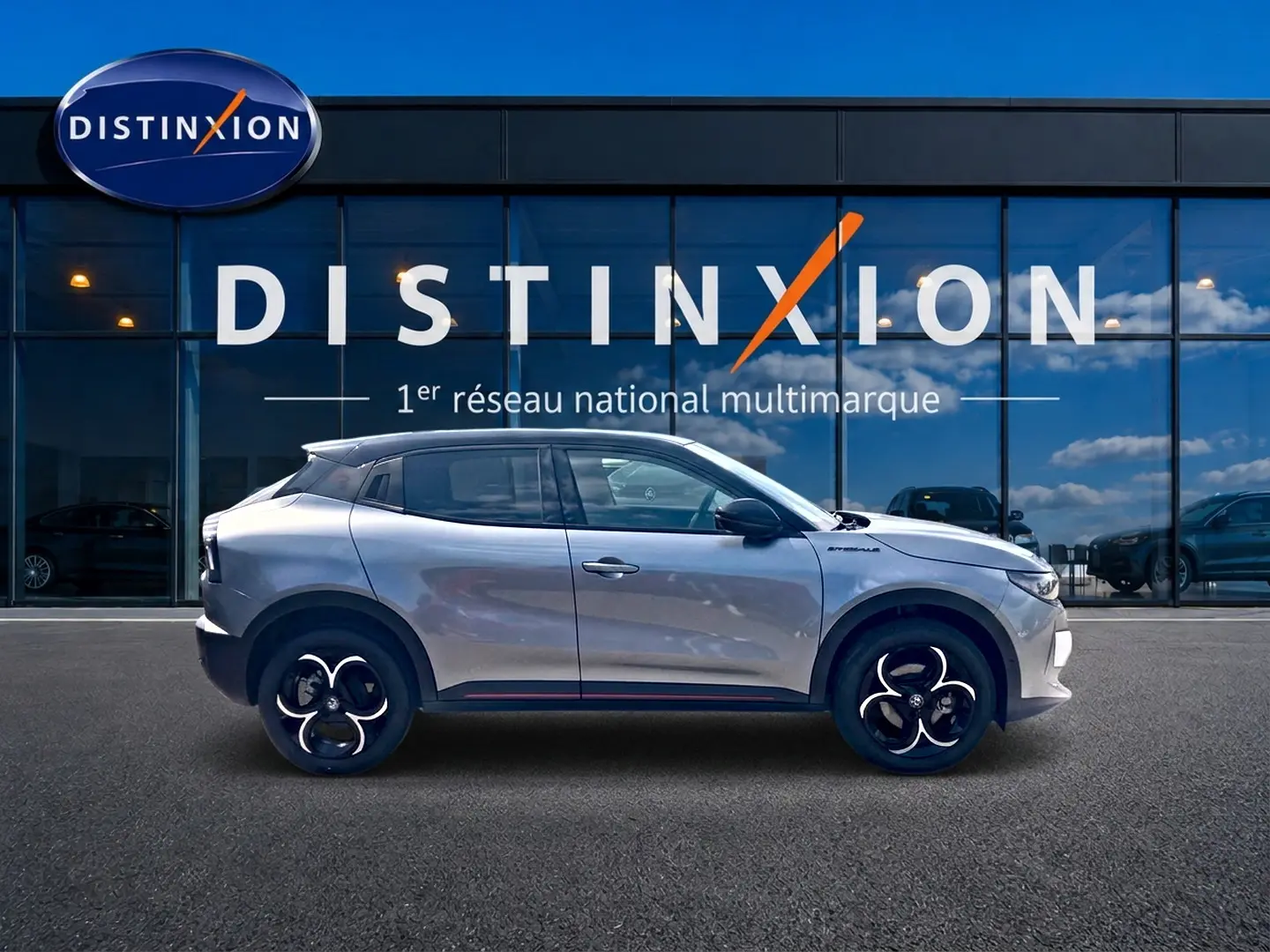 Profil droit d'une Alfa Romeo Junior 1.2 hybride gris foncé avec jantes alliage noires devant une vitrine Distinxion.