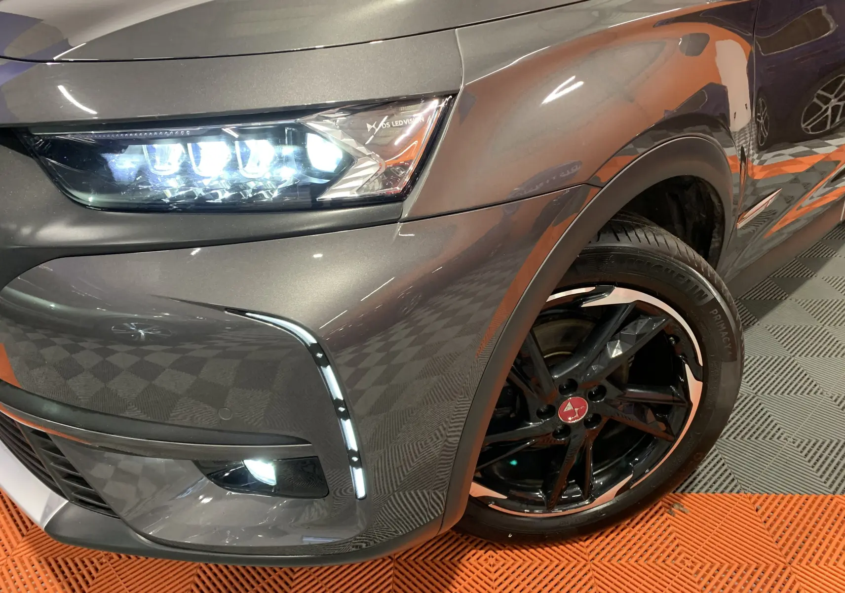 Gros plan sur l'avant droit gris Platinium du DS7 Crossback 2022, mettant en valeur le phare LED et la jante noire à détails blancs.