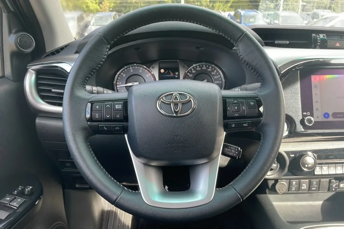 Vue rapprochée du volant multifonction noir du Toyota Hilux 2025, tableau de bord et écran tactile visibles.