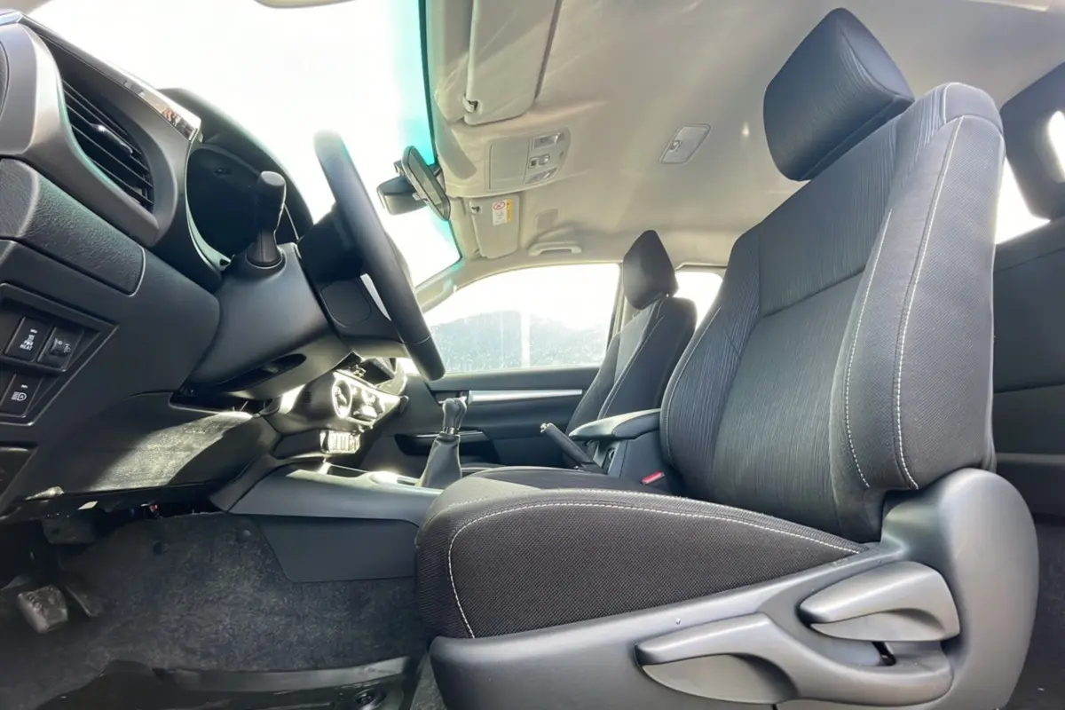 Intérieur du Toyota Hilux 2025 gris acier, vue côté conducteur montrant sièges et tableau de bord avec boîte manuelle.