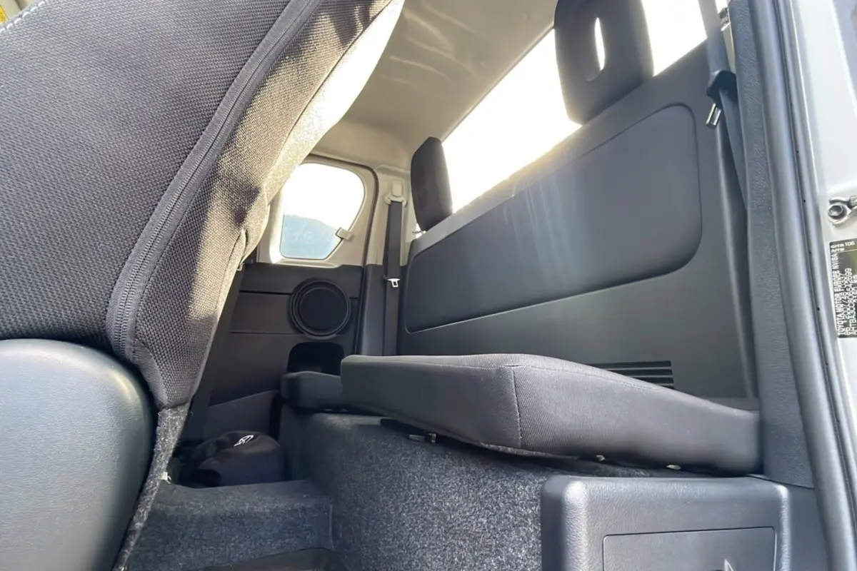 Vue intérieure arrière droite du Toyota Hilux 4x4 gris acier 2025, montrant la banquette rabattue et les finitions en tissu noir.