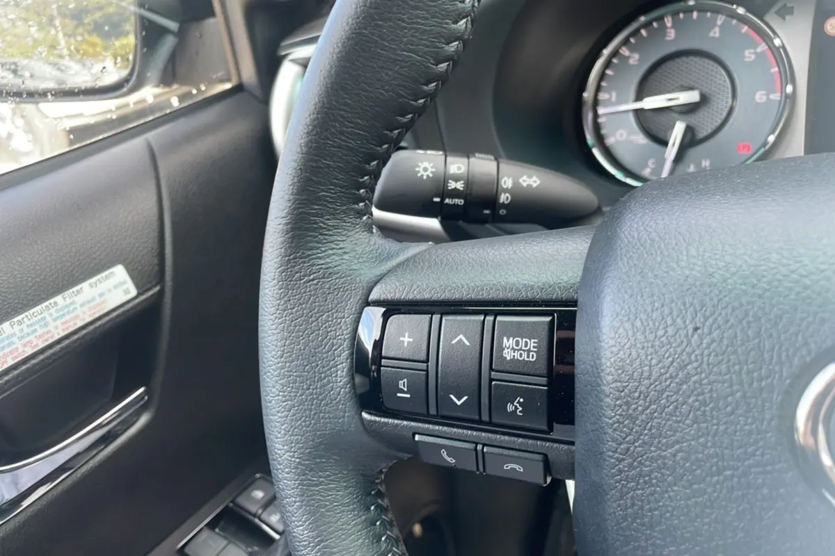 Gros plan sur le volant côté gauche du Toyota Hilux 2025 gris acier, avec commandes audio et tableau de bord en arrière-plan.
