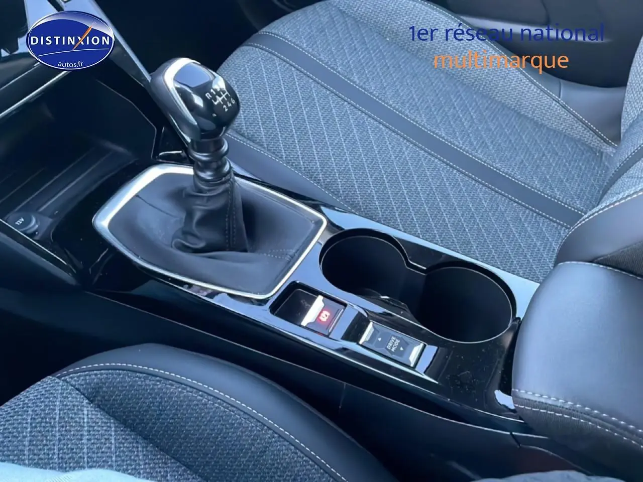 Gros plan sur la console centrale avec levier de vitesses manuel et sièges tissu gris de la Peugeot 208 1.2 100 Allure.