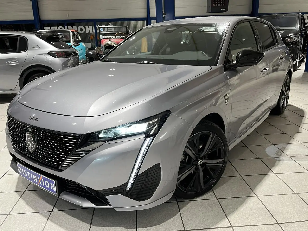 Peugeot 308 gris Artense vue 3/4 avant droit avec calandre noire et jantes alliage 18'' noires en showroom.