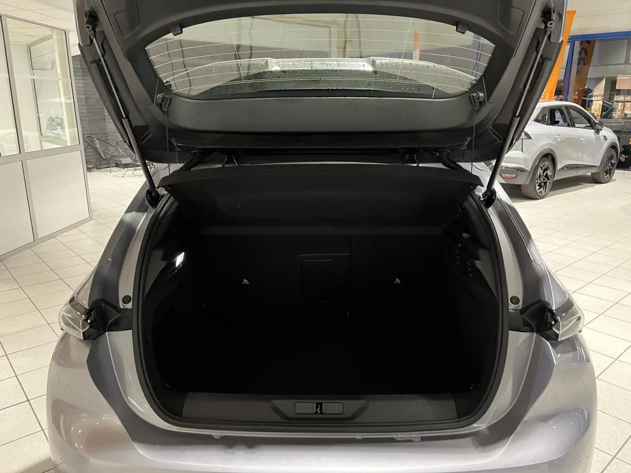 Coffre ouvert vu de l'arrière d'une Peugeot 308 Gris Artense dans un showroom lumineux.
