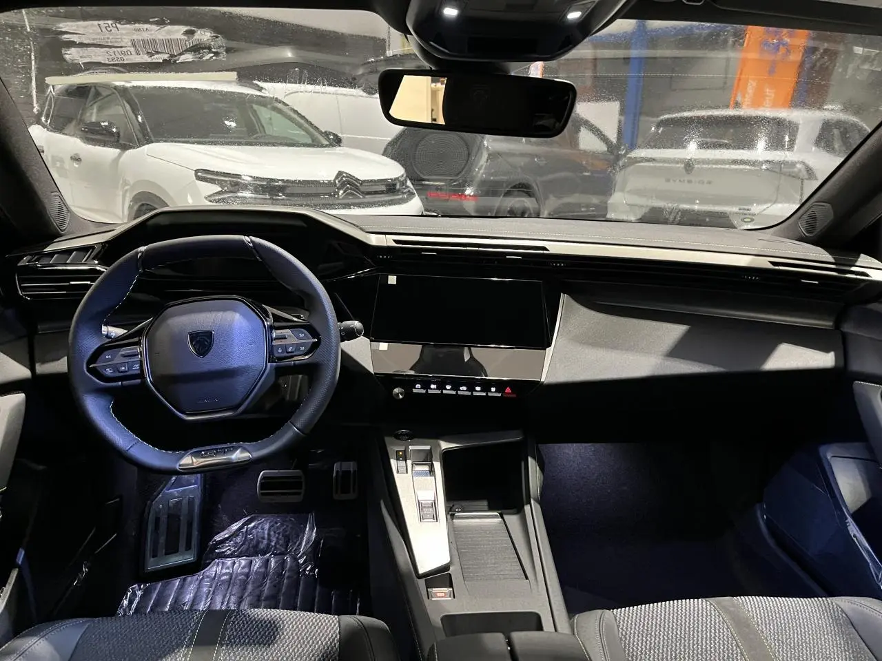 Vue intérieure avant de la Peugeot 308 2024 gris Artense, volant cuir, planche de bord moderne et écran tactile noir.