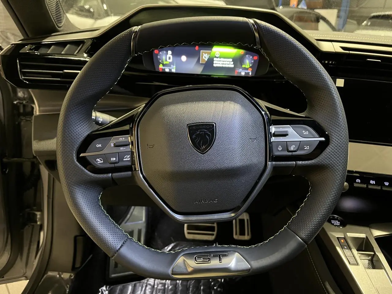 Volant cuir noir GT de la Peugeot 308 2024 vu de face avec combiné numérique et pédaliers aluminium visibles.